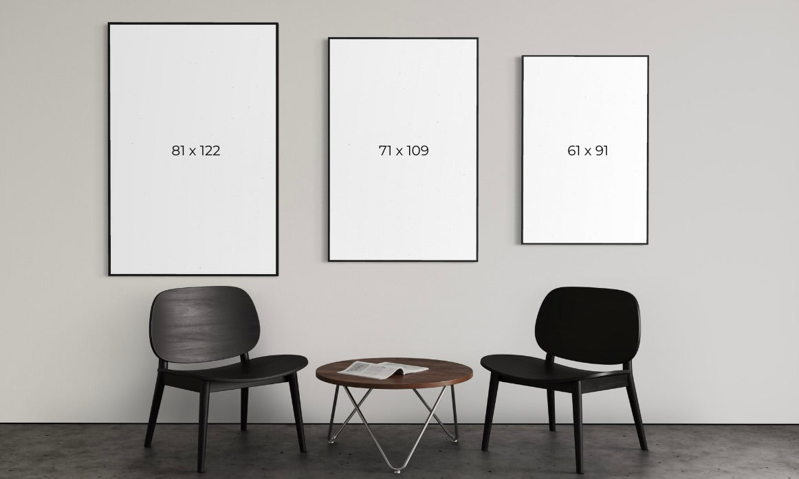 Three framed prints of different sizes on a wall with two chairs and a table below.