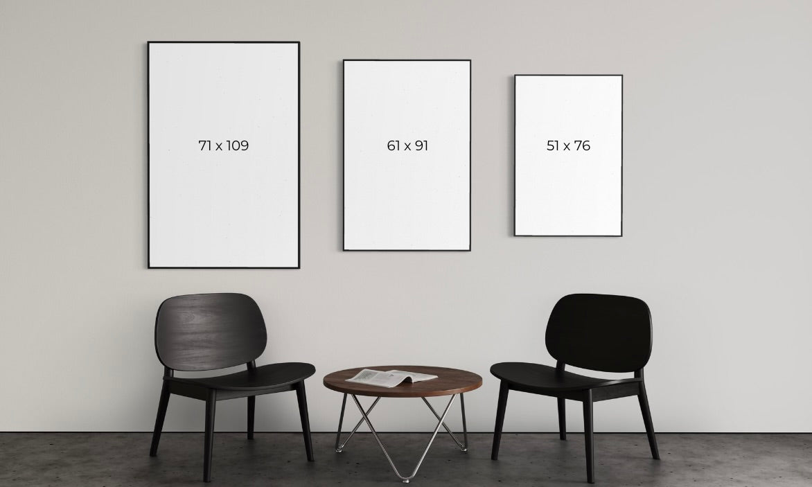 Three framed artworks of different sizes on a wall with two chairs and a table below.