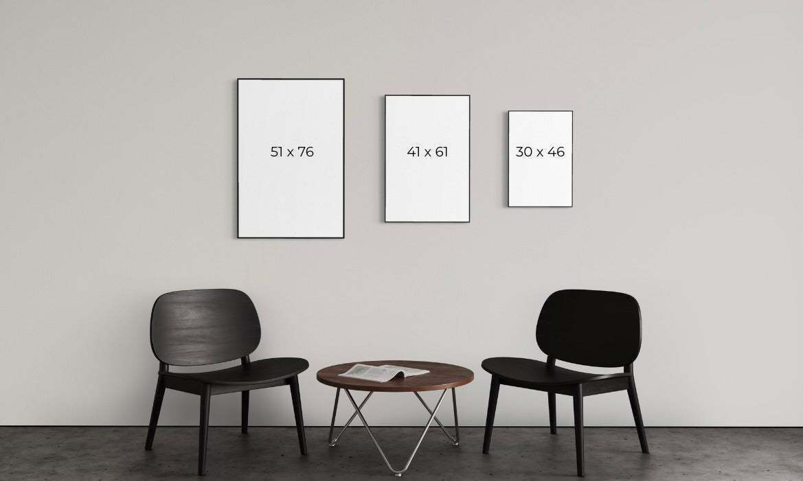 Three framed artworks of different sizes on a wall with two chairs and a table below.