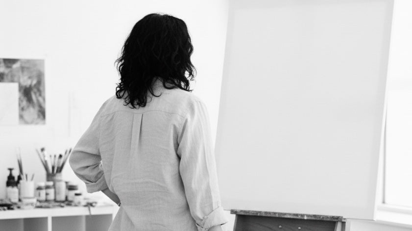 Elizabeth Ortiz standing in a studio with white cabinets and an easel in front of her.