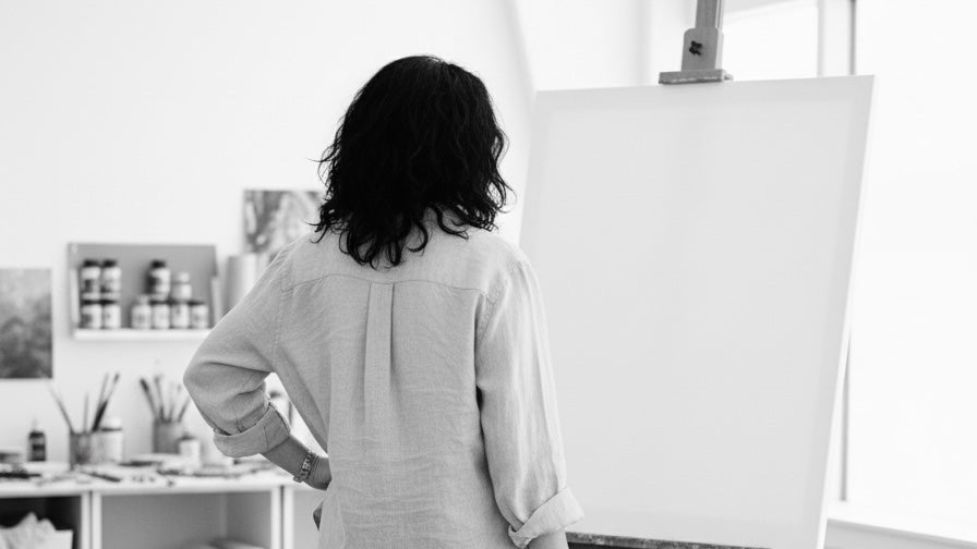 Elizabeth Ortiz standing in front of a blank canvas on an easel in a studio.
