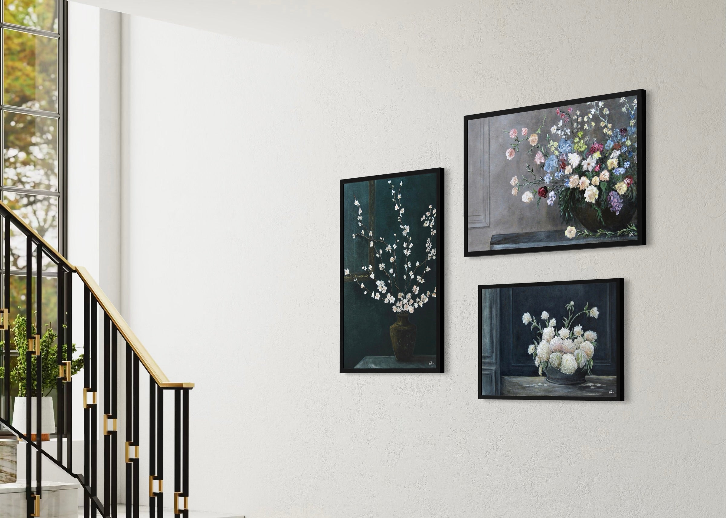 Three framed artworks of floral arrangements on a wall with a staircase in the background.