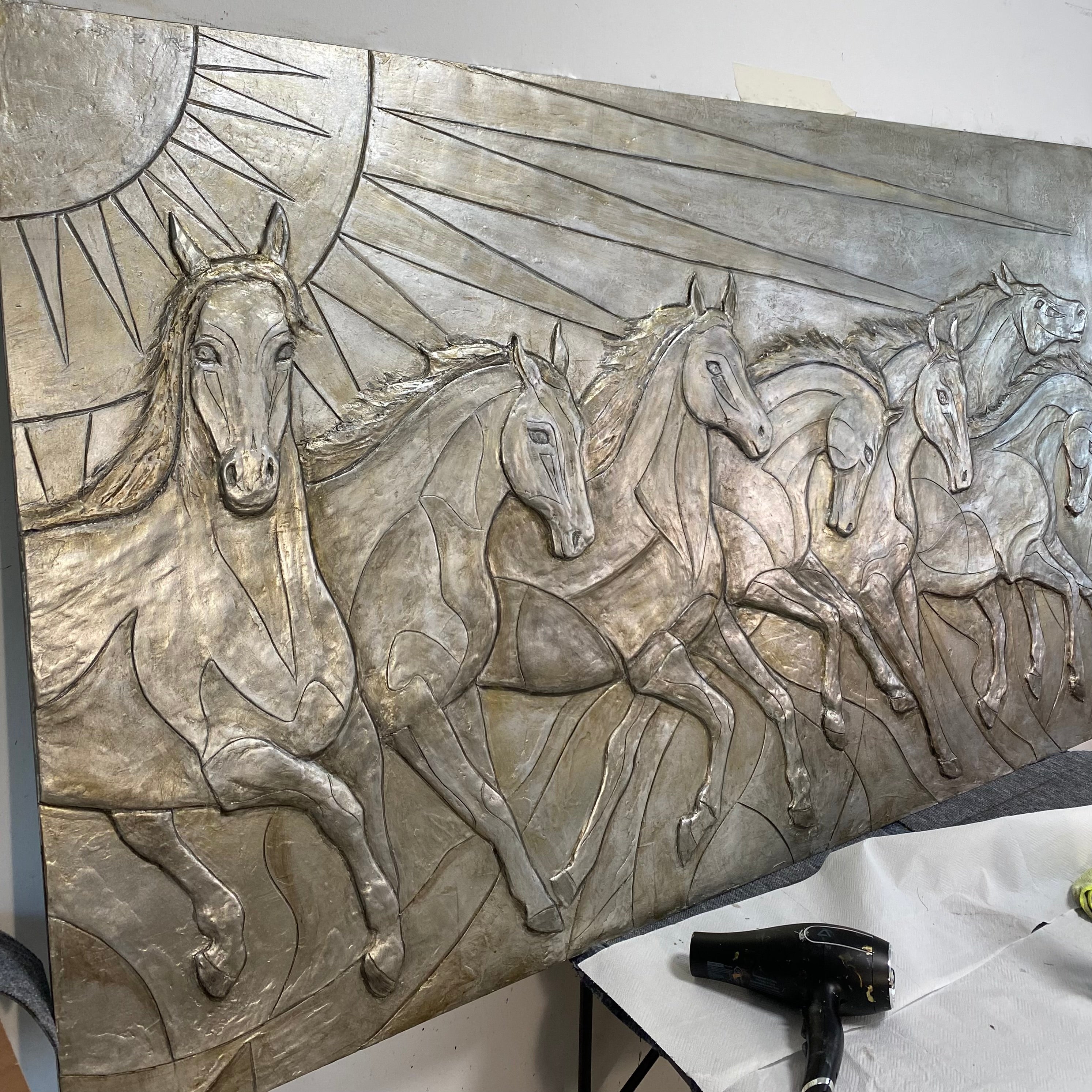 Metallic sculpture of horses running with a sun design in the background