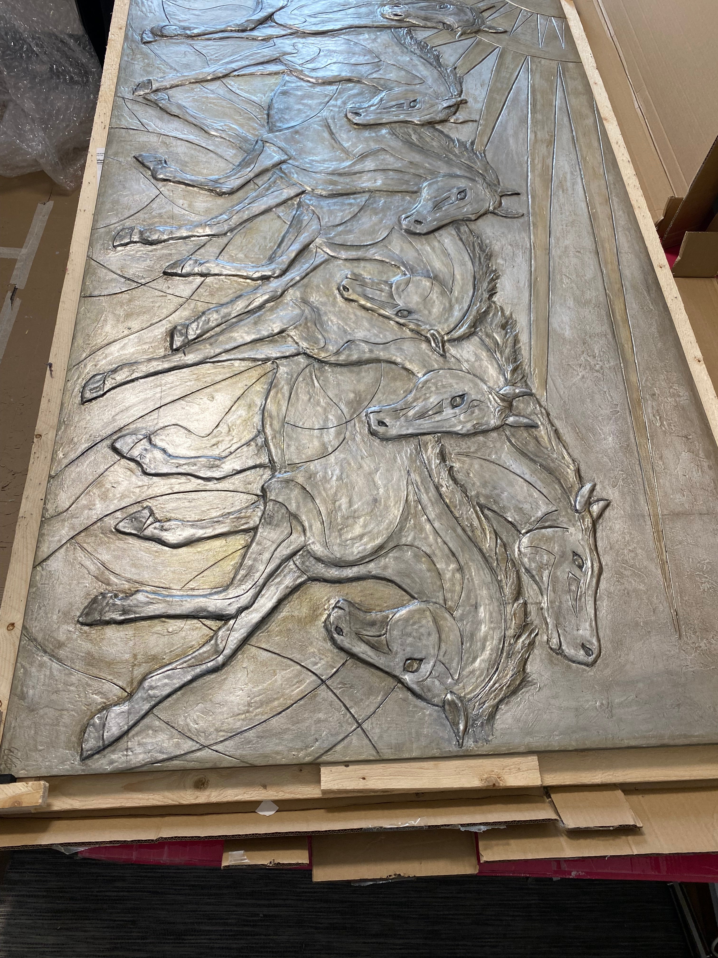 Metallic sculpture of running horses on a textured surface